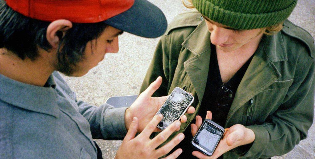 Zwei Männer versuchen, Nummern auszutauschen, aber beide haben Smartphones mit kaputten Displays.